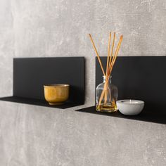 two black shelves with candles, bowl and vase on them next to each other in front of a gray wall