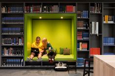 two people sitting on a green couch in front of bookshelves