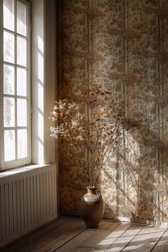 a vase with some flowers in it sitting next to a window on a wooden floor