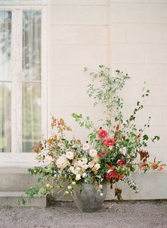 a vase filled with lots of flowers sitting next to a window on the side of a building