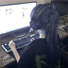 a person wearing headphones sitting in front of a computer keyboard and monitor with long hair