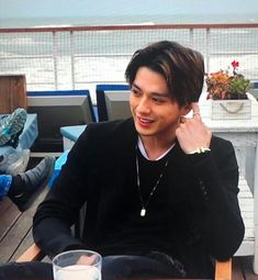 a young man sitting at a table talking on a cell phone and holding his hand up to his ear