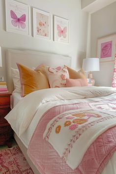 a white bed with pink and orange pillows in a bedroom next to two framed pictures on the wall