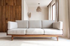 a white couch sitting in front of a window next to a wooden cabinet and lamp