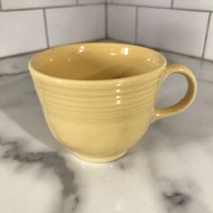 a yellow coffee cup sitting on top of a white marble counter next to a tiled wall