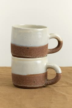 two coffee mugs stacked on top of each other with brown and white glaze