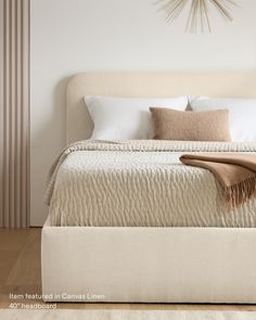 a white bed with pillows and blankets on top of it next to a wall clock