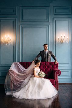 a bride and groom sitting on a red couch in a blue room with chandeliers