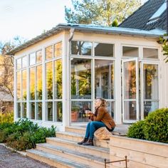 a woman sitting on the steps in front of a house with glass walls and doors