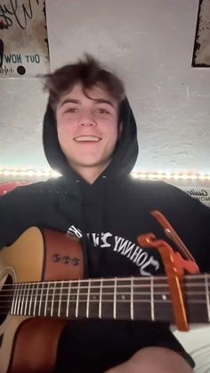 a young man is playing an acoustic guitar in front of the camera and smiling at the camera