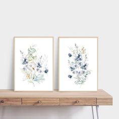 two framed art prints on a wooden shelf next to each other, one with blue and white flowers