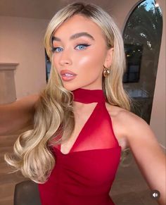 a woman with blonde hair and blue eyes wearing a red halter top, posing for the camera