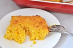 a piece of cornbread on a plate with a fork next to it and a casserole dish in the background