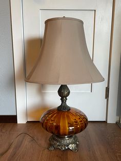 a lamp that is sitting on top of a wooden floor next to a door with a white wall in the background