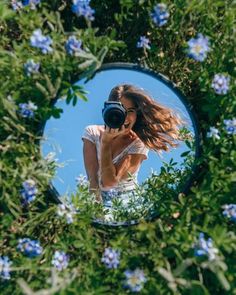 a woman taking a selfie in front of a mirror with blue flowers around her