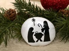 a nativity scene painted on a rock next to pine cones and christmas tree branches