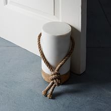 a white vase with a rope around it on the ground next to a door way