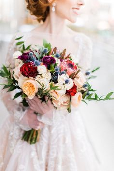 a bride holding a bouquet of flowers in her hand and looking off into the distance