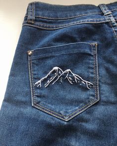 a pair of blue jeans with mountains embroidered on them