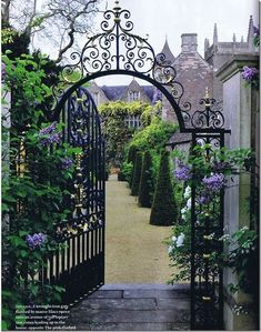 an iron gate with flowers growing on the sides and in between it is a stone walkway