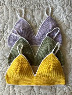 three knitted bras on top of a quilted bedspread, one in green, the other in purple and yellow