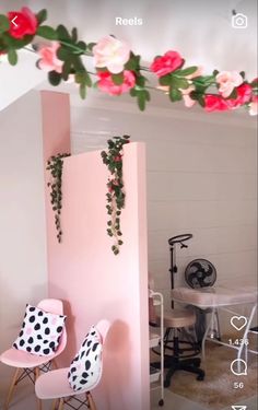 two pink chairs are in front of a wall with flowers hanging from it and the floor is tiled