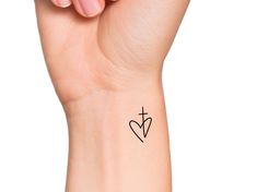 a woman's wrist with a cross and heart tattoo on the left side of her arm