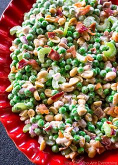 a red bowl filled with peas, bacon and other food items on top of it