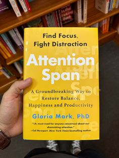 a person holding up a yellow book in front of a bookshelf