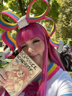 a woman with pink hair is holding a book in front of her face and wearing a mouse ears headband