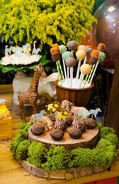 a table topped with cake pops covered in animals and jungle themed food items on top of a tree stump