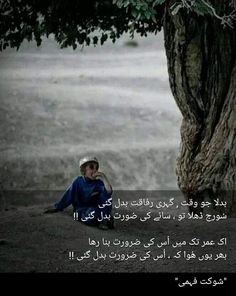 a young boy sitting under a tree in front of a field