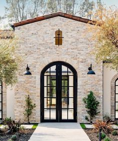 a brick building with black doors and glass windows on the front door is surrounded by greenery