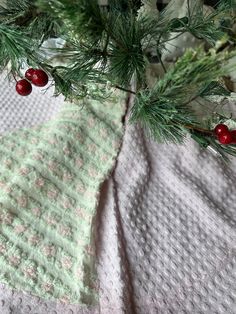 a close up of a knitted blanket on a table with pine needles and red berries