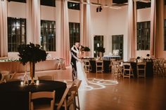 a bride and groom are standing in the middle of a room with tables, chairs, and chandeliers