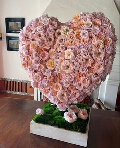 a large heart made out of pink flowers on top of a wooden table with moss