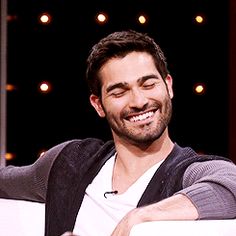 a smiling man sitting in a chair with his arms crossed and looking at the camera