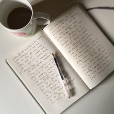 an open book with writing on it next to a cup of coffee and a pen