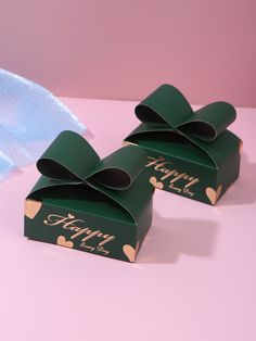 two green boxes with gold hearts on them sitting next to a blue bow and ribbon