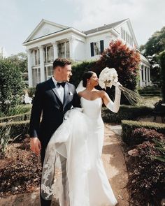 a bride and groom walking in front of a house