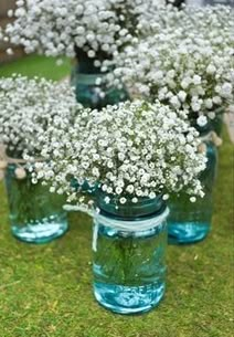 four mason jars with baby's breath flowers in them on the grass near some bushes