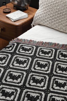 a black and white crocheted blanket on top of a bed next to a night stand