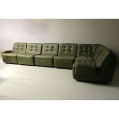 a green leather sectional sofa sitting on top of a white floor next to a lamp