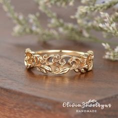 a gold ring with leaves on it sitting on a wooden table next to some flowers