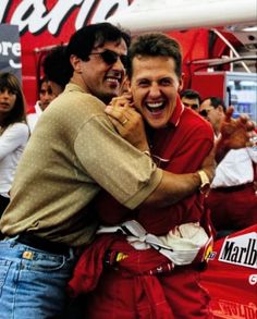 two men are hugging each other in front of a red sign and some people behind them