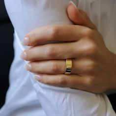 a woman's hand with a gold ring on her left wrist, wearing a white shirt