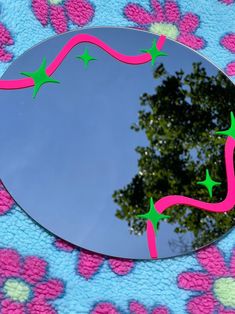 the reflection of a tree in a mirror with pink and green stars on it's side