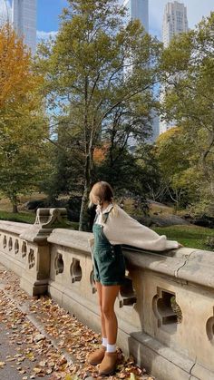 a woman leaning on a stone wall in the park with her head down and looking at something