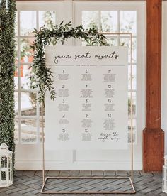 a wedding seating chart with greenery on the side and white chairs at the back