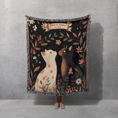 a woman standing in front of a tapestry with two cats on it's back